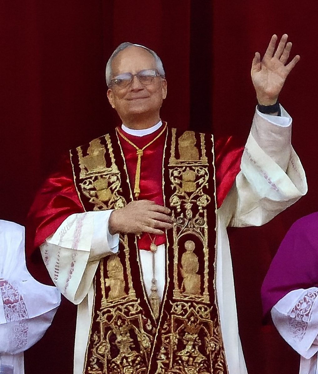 Papa Leone XIV sorride e saluta con la mano alzata, con la mozzetta rossa e la stola, il giorno della sua elezione.
